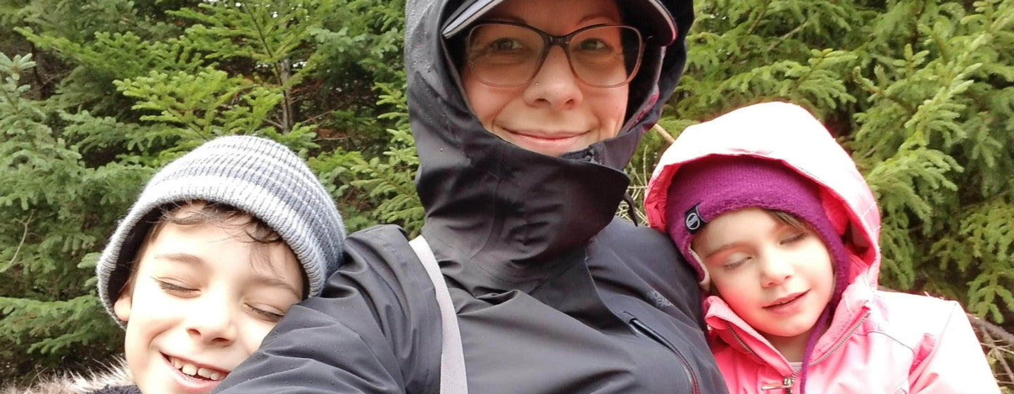 Image contains a photo of a woman, Dee Loft, in a raincoat in the center. On her right and left, there are two small children smiling with their eyes closed.
