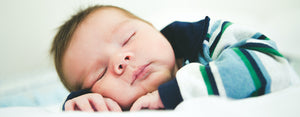 Image contains a photo of a baby sleeping on a white blanket or sheet.