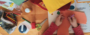 Image contains a photo of a child being educated in fun ways involving construction paper, scissors, pencils, and other things.
