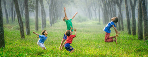 Image contains a photo of four young children developing healthy habits by playing in a forest.