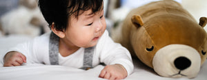 Image contains a photo of a young child laying down next to a stuffed teddy bear.
