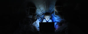 Image contains a photo of a toddler in a dark room looking at a screen. Their parents are sitting on each side reading newspapers.