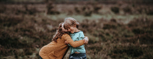 Image contains a photo of a smiling kid being hugged by a friend.