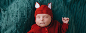 Image contains a photo of a baby sleeping in a red fox onesie as an illustration of how sleep affects development.