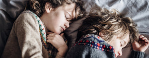 Image contains a photo of two toddlers sleeping next to each other in a bed.